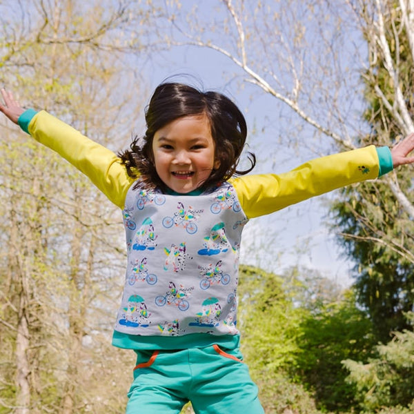 Image of a happy child leaping in the air with her arms open wide, wearing a Ducky Zebra jumper