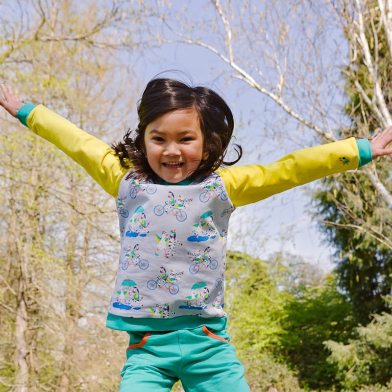 Image of a happy child leaping in the air with her arms open wide, wearing a Ducky Zebra jumper