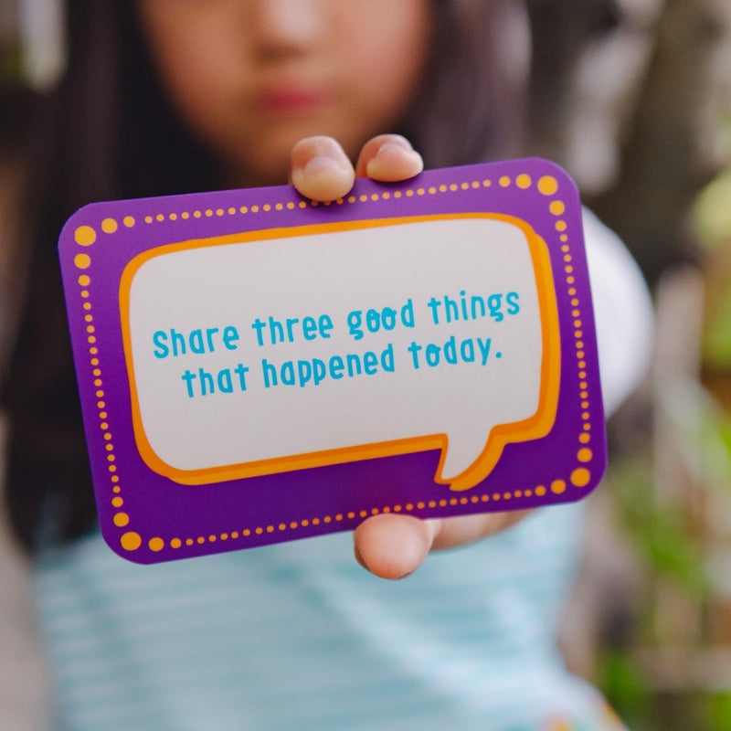 Image of a girl holding one of the Happy Confident Company Conversation Cards, which states "share three good things that happened today."