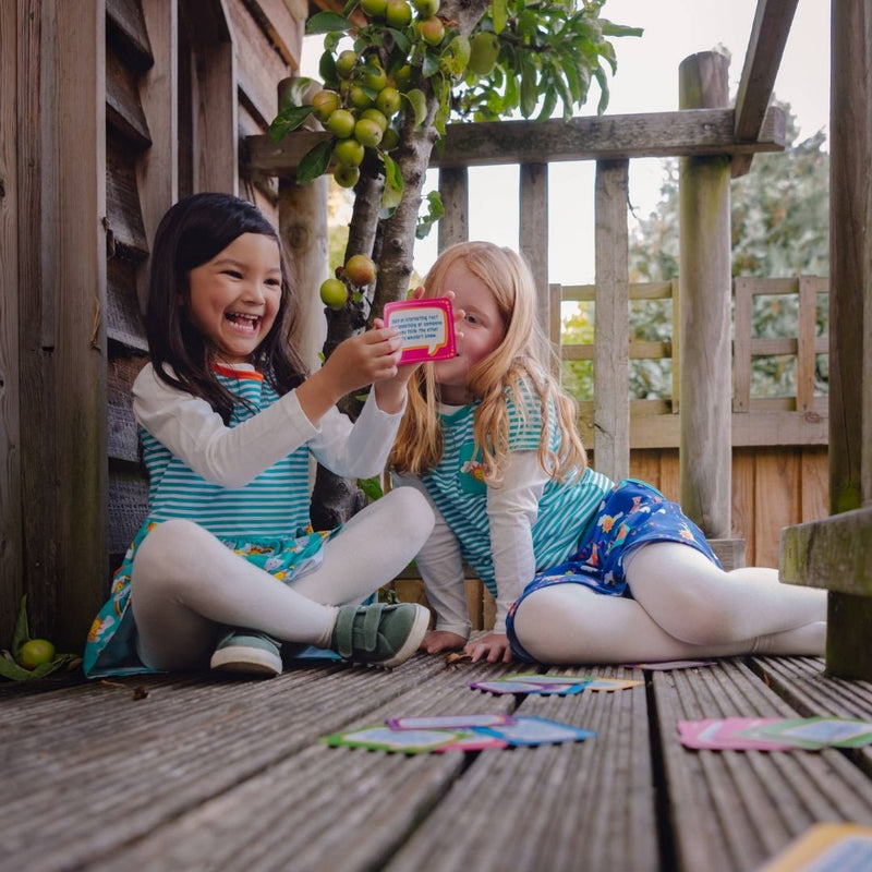 Image of two happy children sitting in a tree house, wearing Ducky Zebra clothes, playing with the Conversation Cards 