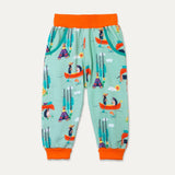 Ducky Zebra unisex green kids trousers with a fun, colourful print of a canoeing dog and hedgehog. The trousers have two deep pockets and an orange waistband and roll-up cuff.