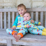 Image of a brother and sister sitting on a bench wearing Ducky Zebra twinning outfits. The brother has a canoeing dog and hedgehog print sweatshirt and joggers. And the baby sister is wearing a canoeing dog and hedgehog print romper.