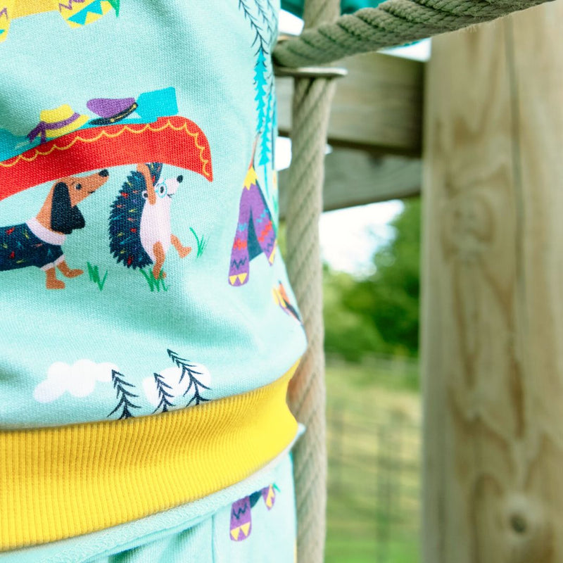 Close up of a green unisex kids Ducky Zebra jumper - focusing on the print of a dog and hedgehog holding a canoe over their heads