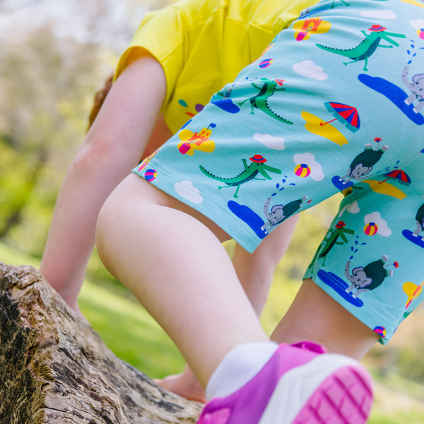 Child confidently climbing a tree, wearing a pair of Ducky Zebra seaside print shorts with a yellow t-shirt
