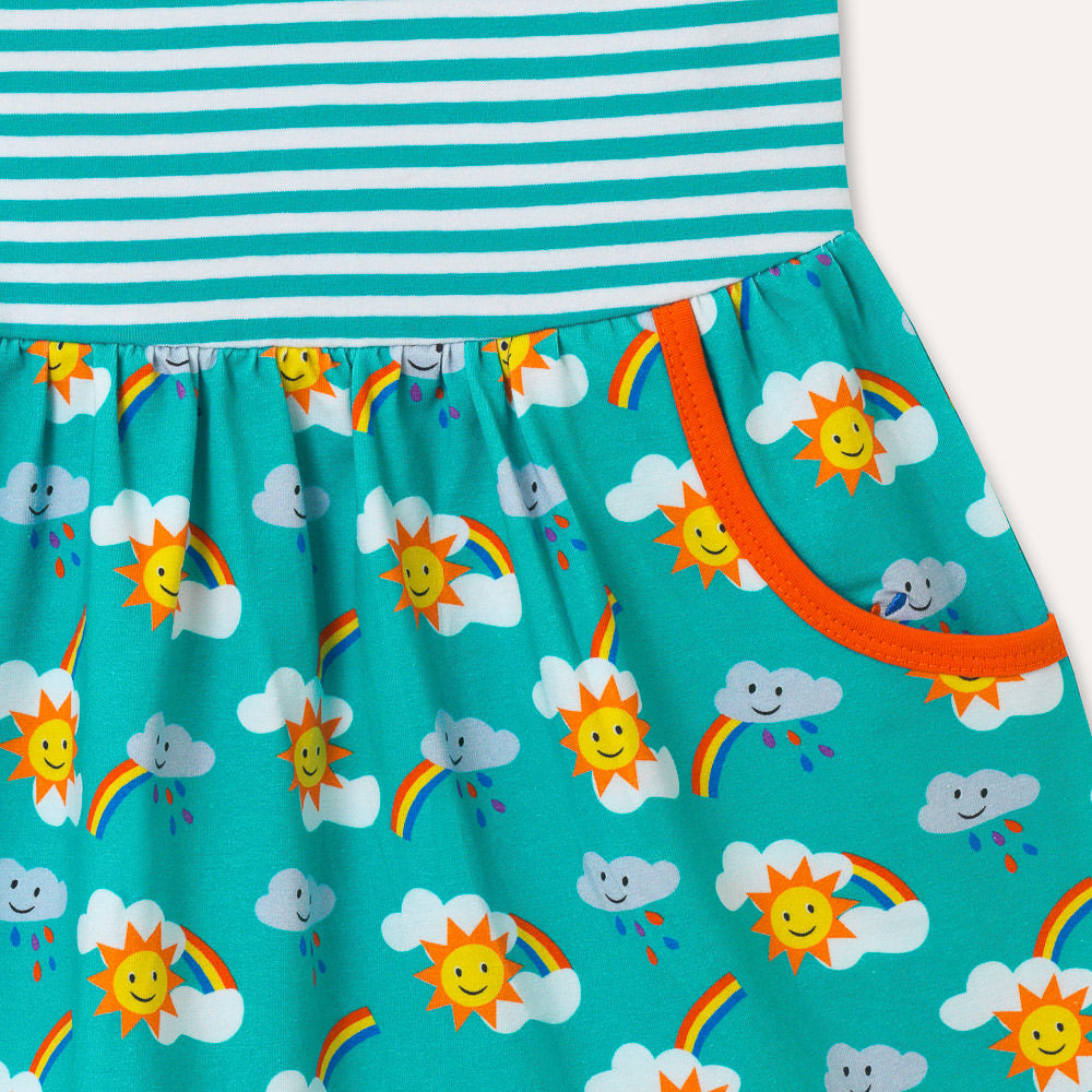 Image of sleeveless kids dress with turquoise stripe top half and rainbow print bottom half, focusing on one of the two large pockets with an orange trim