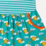 Image of sleeveless kids dress with turquoise stripe top half and rainbow print bottom half, focusing on one of the two large pockets with an orange trim