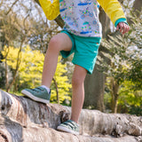 Image of a child balancing along a fallen tree wearing a pair of unisex turquoise shorts and a Ducky Zebra sweatshirt