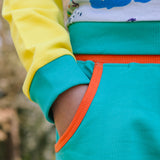Image of child's hand inside the pocket of a pair of unisex turquoise shorts with an orange pocket trim.