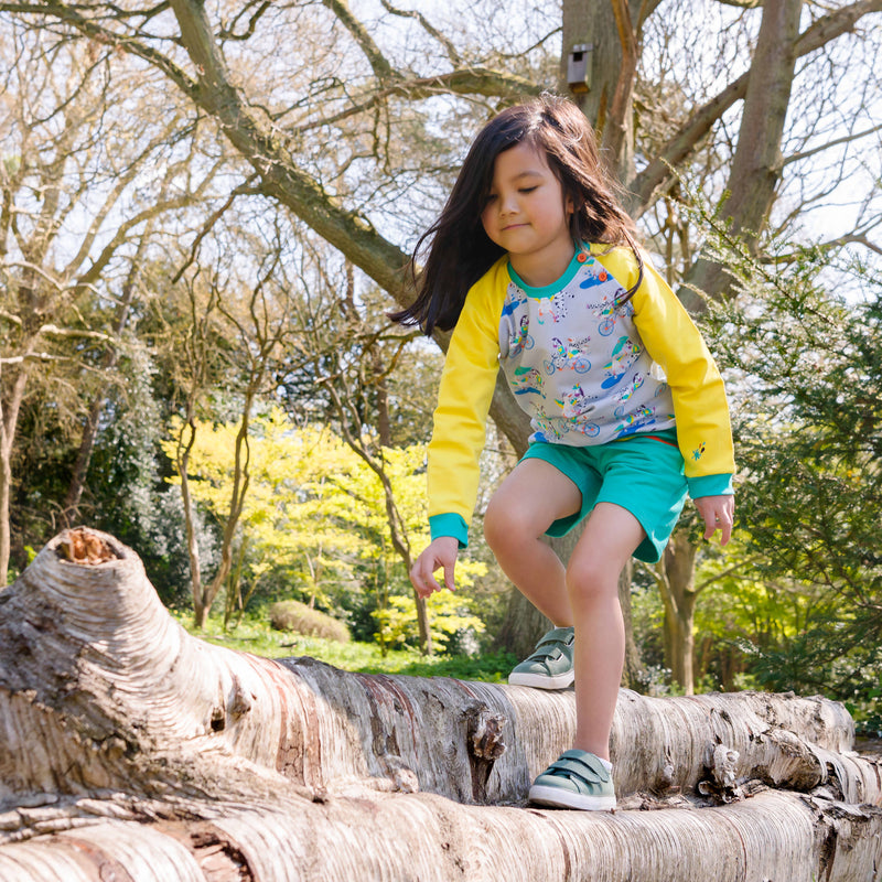 Image of a girl climbing on a fallen tree, wearing a Ducky Zebra jumper and turquoise shorts 