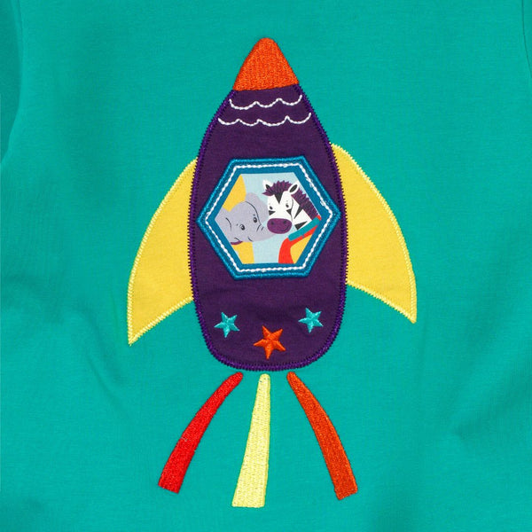 Close up of a rocket applique - with an elephant and zebra peeking out of the window. The rocket is purple, yellow and orange and the background is turquoise.