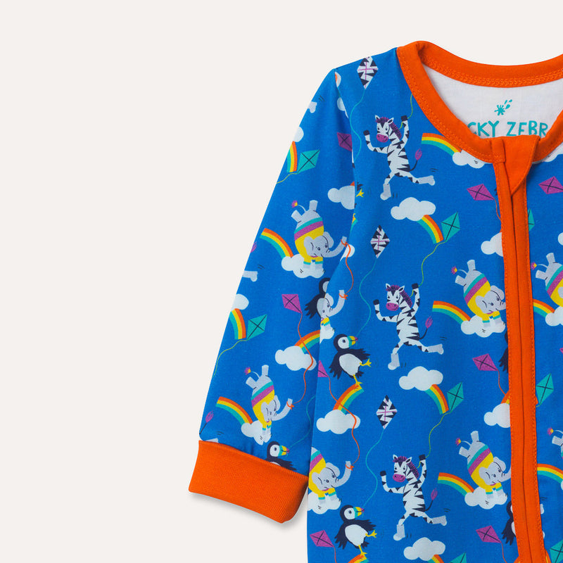 Image of a long sleeve zip-up unisex baby romper with a bright blue background and colourful repeat print pattern of an elephant, zebra and puffin flying a kite. The image focuses on the top half of the romper and shows the flame orange arm cuffs, trim and two way zip