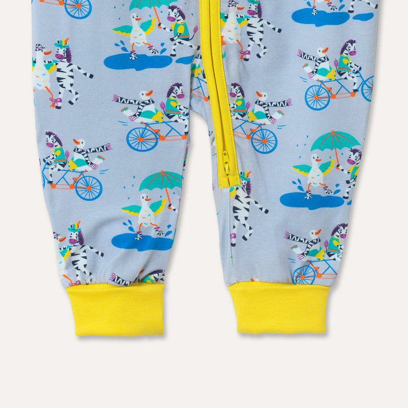 Image of a zip-up unisex baby romper with a light grey background and colourful repeat print pattern of a duck and zebra splashing in a puddle, riding a bicycle and running a three legged race. The images shows bright yellow roll up cuffs and a two way zip
