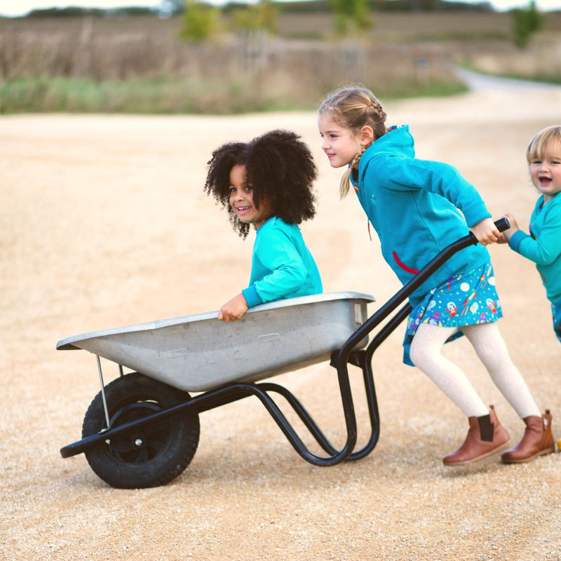 Children playing in a wheelbarrow. All of the children are wearing colourful, sustainable Ducky Zebra clothes from their space collection including their teal hoodie.