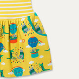 Close up image of a Ducky Zebra sleeveless dress. The dress has a yellow and white stripe top half with a printed bottom half. The print has a yellow background with a crocodile and elephant enjoying a hot air balloon ride and playing together in the leaves.