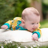 Image of baby lying on its front on top of a cushion in the grass. The baby is smiling and wearing a Ducky Zebra baby sleepsuit.