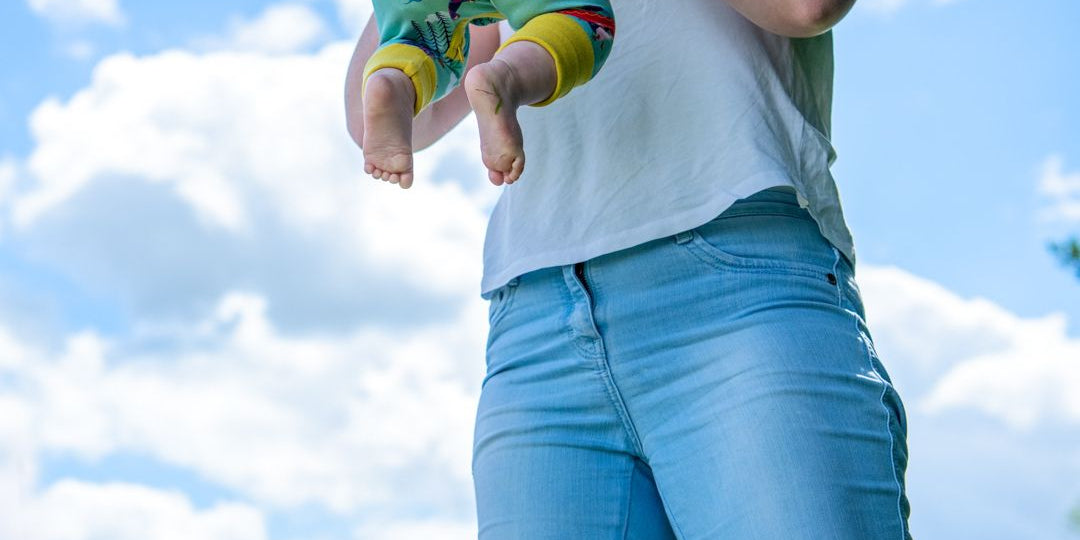 Image of a mum throwing up their baby into the air. The baby is wearing a Ducky Zebra baby romper.