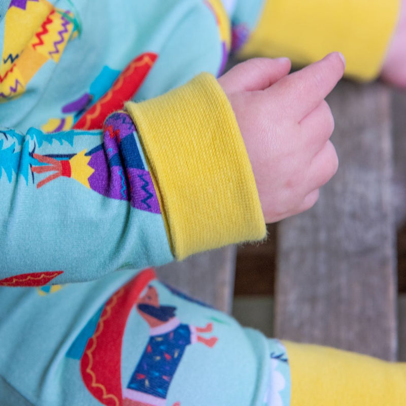 Close up image of a baby's arms and hands. The baby is wearing a Ducky Zebra romper, with the yellow cuffs rolled up.