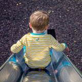 Image of the back of a child sliding down a slide. The child is wearing a Ducky Zebra long-sleeve t-shirt. The t-shirt has yellow and white stripes and an embroidered splash power button on the back, below the neck-line. 