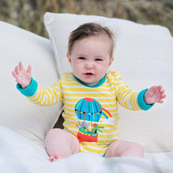 Image of a baby wearing a Ducky Zebra yellow and white stripe baby bodysuit with a turquoise trim and cuffs. The bodysuit has an image of a hot air balloon on the centre front, with a crocodile and elephant in the basket. 