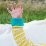 Image of a baby's arm waving. The baby is wearing a yellow and white Ducky Zebra bodysuit